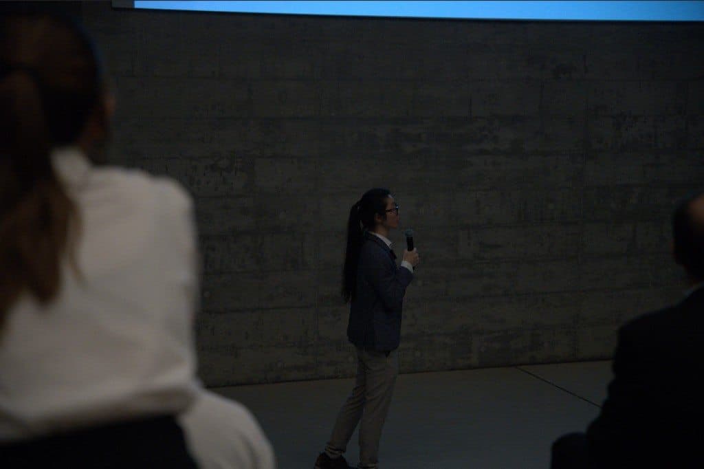 Adam speaking with a microphone in a concrete auditorium